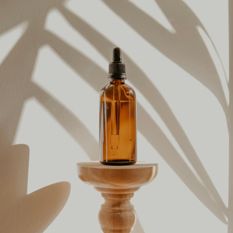 fragrance oil bottle on pedestal with shadows of plants and sunlight